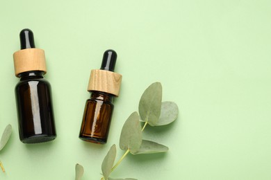 Photo of Bottles of essential oil and eucalyptus leaves on green background, flat lay. Space for text