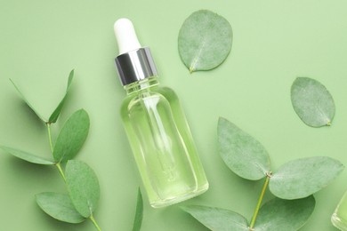Photo of Bottle of essential oil and eucalyptus leaves on green background, flat lay