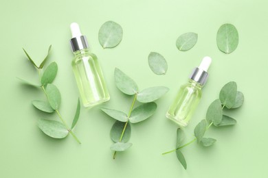 Photo of Bottles of essential oil and eucalyptus leaves on green background, flat lay