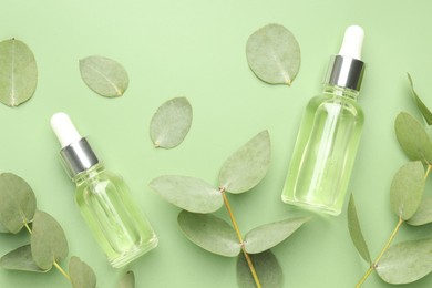 Photo of Bottles of essential oil and eucalyptus leaves on green background, flat lay
