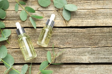 Photo of Bottles of essential oil and eucalyptus leaves on wooden table, flat lay. Space for text
