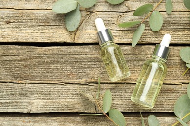 Photo of Bottles of essential oil and eucalyptus leaves on wooden table, flat lay. Space for text