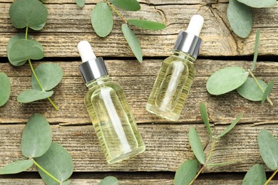 Photo of Bottles of essential oil and eucalyptus leaves on wooden table, flat lay