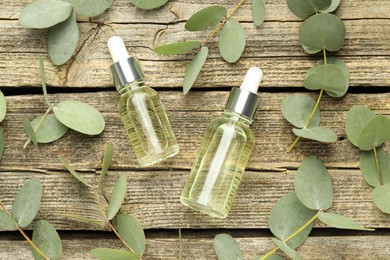 Photo of Bottles of essential oil and eucalyptus leaves on wooden table, flat lay