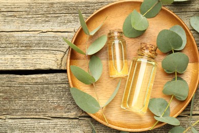 Photo of Bottles of essential oil and eucalyptus leaves on wooden table, flat lay. Space for text