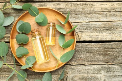 Photo of Bottles of essential oil and eucalyptus leaves on wooden table, flat lay. Space for text
