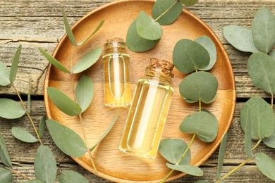 Photo of Bottles of essential oil and eucalyptus leaves on wooden table, flat lay