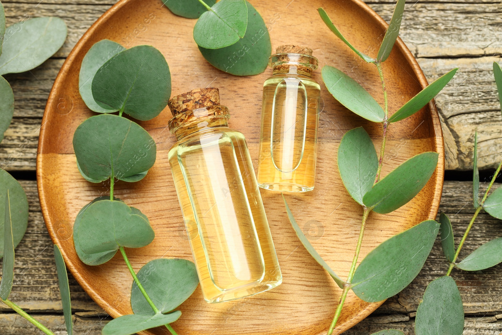 Bottles of essential oil and eucalyptus leaves on wooden table, flat lay Photo of Bottles of essential oil and eucalyptus leaves on wooden table, flat lay