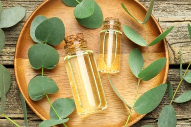 Photo of Bottles of essential oil and eucalyptus leaves on wooden table, flat lay