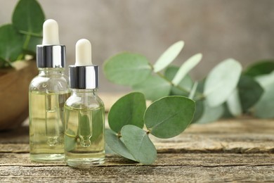 Photo of Bottles of essential oil and eucalyptus leaves on wooden table, closeup