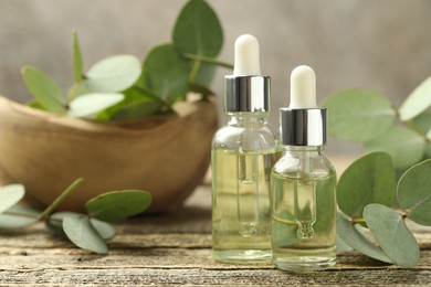 Photo of Bottles of essential oil and eucalyptus leaves on wooden table, closeup