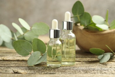 Photo of Bottles of essential oil and eucalyptus leaves on wooden table, closeup