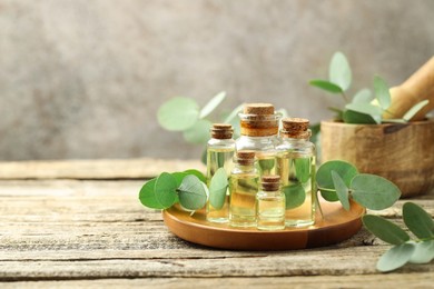 Photo of Bottles of essential oil, eucalyptus leaves, mortar and pestle on wooden table, space for text