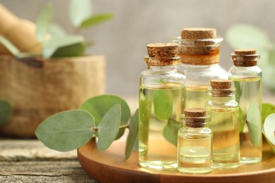 Photo of Bottles of essential oil and eucalyptus leaves on wooden table, closeup