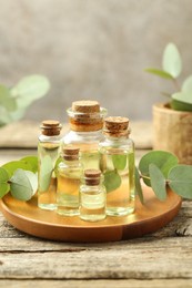 Photo of Bottles of essential oil and eucalyptus leaves on wooden table, closeup