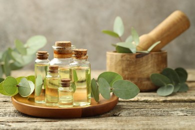 Photo of Bottles of essential oil, eucalyptus leaves, mortar and pestle on wooden table