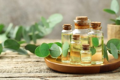 Photo of Bottles of essential oil and eucalyptus leaves on wooden table, closeup. Space for text