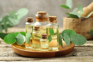 Photo of Bottles of essential oil and eucalyptus leaves on wooden table, closeup