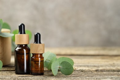 Photo of Bottles of essential oil and eucalyptus leaves on wooden table, closeup. Space for text