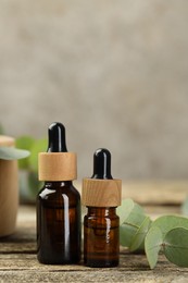 Photo of Bottles of essential oil and eucalyptus leaves on wooden table, closeup