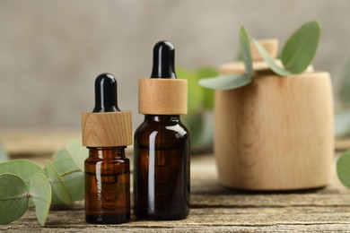 Photo of Bottles of essential oil and eucalyptus leaves on wooden table, closeup
