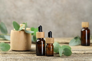 Photo of Bottles of essential oil and eucalyptus leaves on wooden table