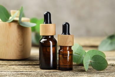 Photo of Bottles of essential oil and eucalyptus leaves on wooden table, closeup