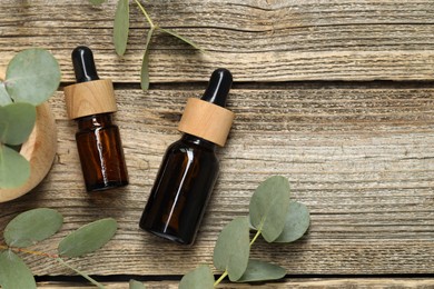 Photo of Bottles of essential oil and eucalyptus leaves on wooden table, flat lay. Space for text