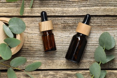 Photo of Bottles of essential oil and eucalyptus leaves on wooden table, flat lay