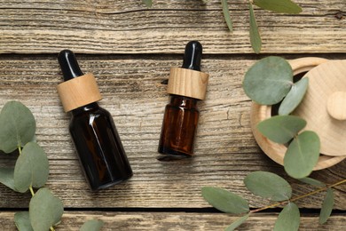 Photo of Bottles of essential oil and eucalyptus leaves on wooden table, flat lay
