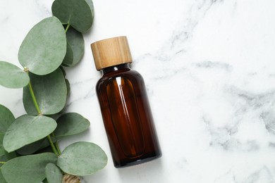 Photo of Bottle of essential oil and eucalyptus leaves on white marble table, flat lay. Space for text