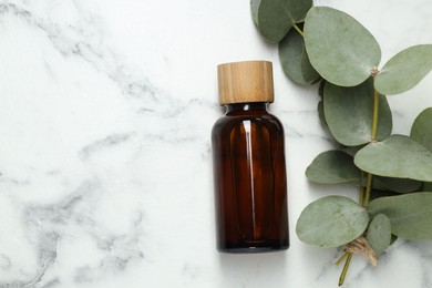 Photo of Bottle of essential oil and eucalyptus leaves on white marble table, flat lay. Space for text