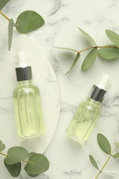 Photo of Bottles of essential oil and eucalyptus leaves on white marble table, flat lay