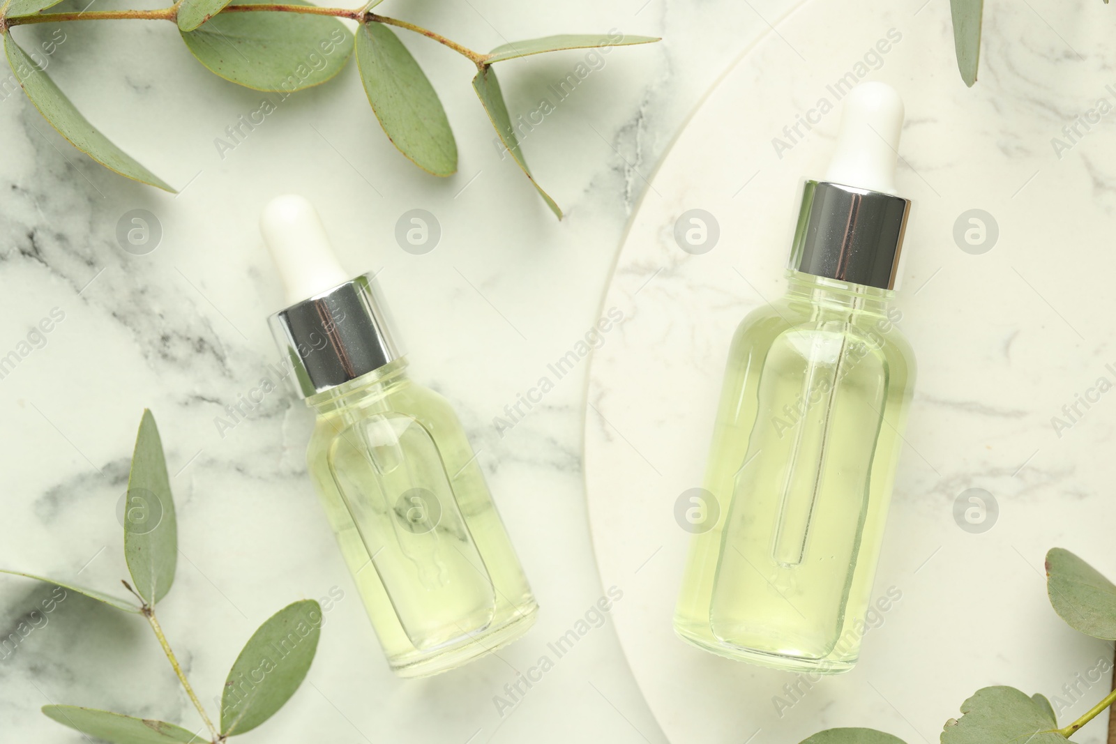 Bottles of essential oil and eucalyptus leaves on white marble table, flat lay Photo of Bottles of essential oil and eucalyptus leaves on white marble table, flat lay