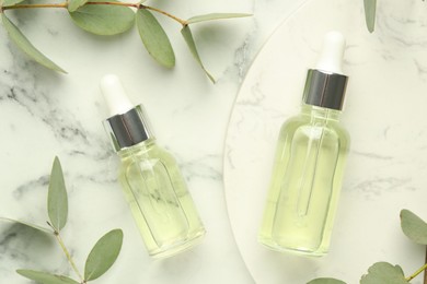 Photo of Bottles of essential oil and eucalyptus leaves on white marble table, flat lay