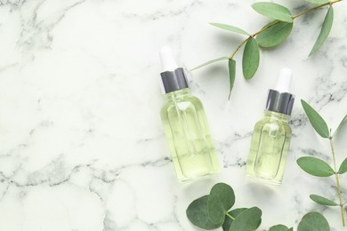Photo of Bottles of essential oil and eucalyptus leaves on white marble table, flat lay. Space for text