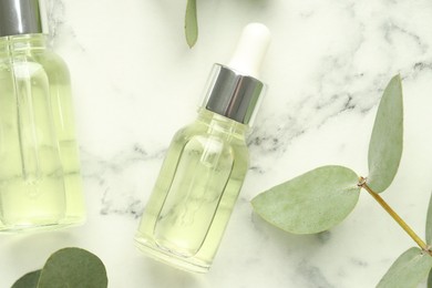 Photo of Bottles of essential oil and eucalyptus leaves on white marble table, flat lay
