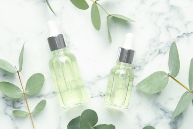 Photo of Bottles of essential oil and eucalyptus leaves on white marble table, flat lay