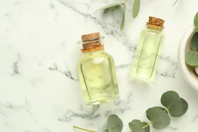 Photo of Bottles of essential oil and eucalyptus leaves on white marble table, flat lay