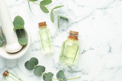 Photo of Bottles of essential oil, eucalyptus leaves, mortar and pestle on white marble table, flat lay. Space for text