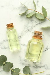 Photo of Bottles of essential oil, eucalyptus leaves, mortar and pestle on white marble table, flat lay