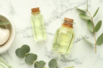 Photo of Bottles of essential oil, eucalyptus leaves, mortar and pestle on white marble table, flat lay