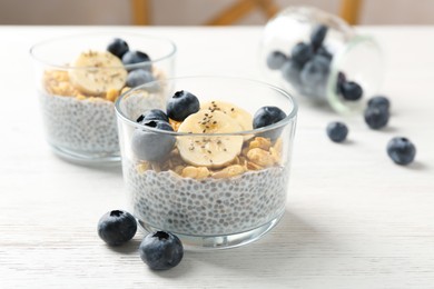 Photo of Delicious dessert with chia seeds, yogurt, granola, blueberries and banana on white wooden table, closeup. Superfood
