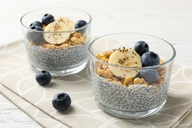 Photo of Delicious dessert with chia seeds, yogurt, granola, blueberries and banana on white wooden table, closeup. Superfood