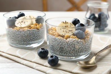 Photo of Delicious dessert with chia seeds, yogurt, granola, blueberries and banana on white wooden table, closeup. Superfood