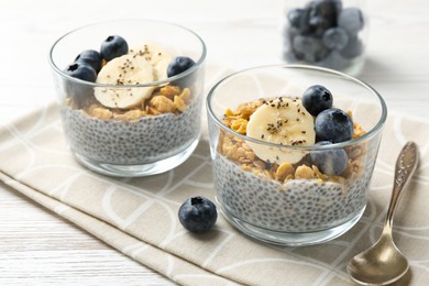 Photo of Delicious dessert with chia seeds, yogurt, granola, blueberries and banana on white wooden table, closeup. Superfood
