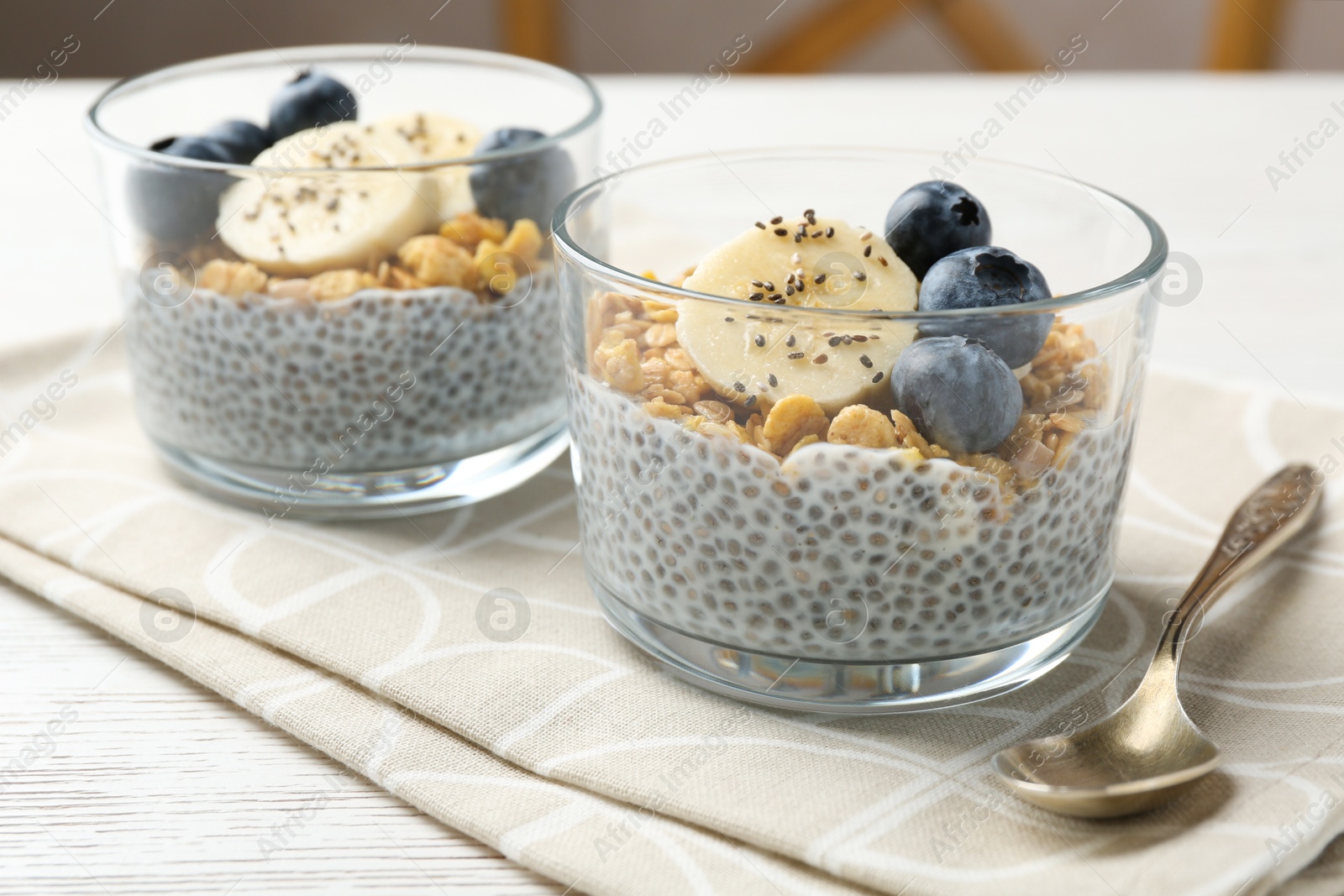 Delicious dessert with chia seeds, yogurt, granola, blueberries and banana on white wooden table, closeup. Superfood Photo of Delicious dessert with chia seeds, yogurt, granola, blueberries and banana on white wooden table, closeup. Superfood
