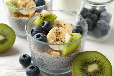 Photo of Delicious dessert with chia seeds, yogurt, granola, blueberries, banana and kiwi on white wooden table, closeup. Superfood