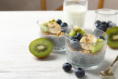 Photo of Superfood. Delicious dessert with chia seeds, yogurt, granola, blueberries, banana and kiwi on white wooden table, closeup. Space for text
