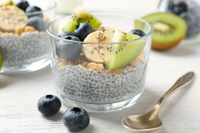 Photo of Delicious dessert with chia seeds, yogurt, granola, blueberries, banana and kiwi on white wooden table, closeup. Superfood